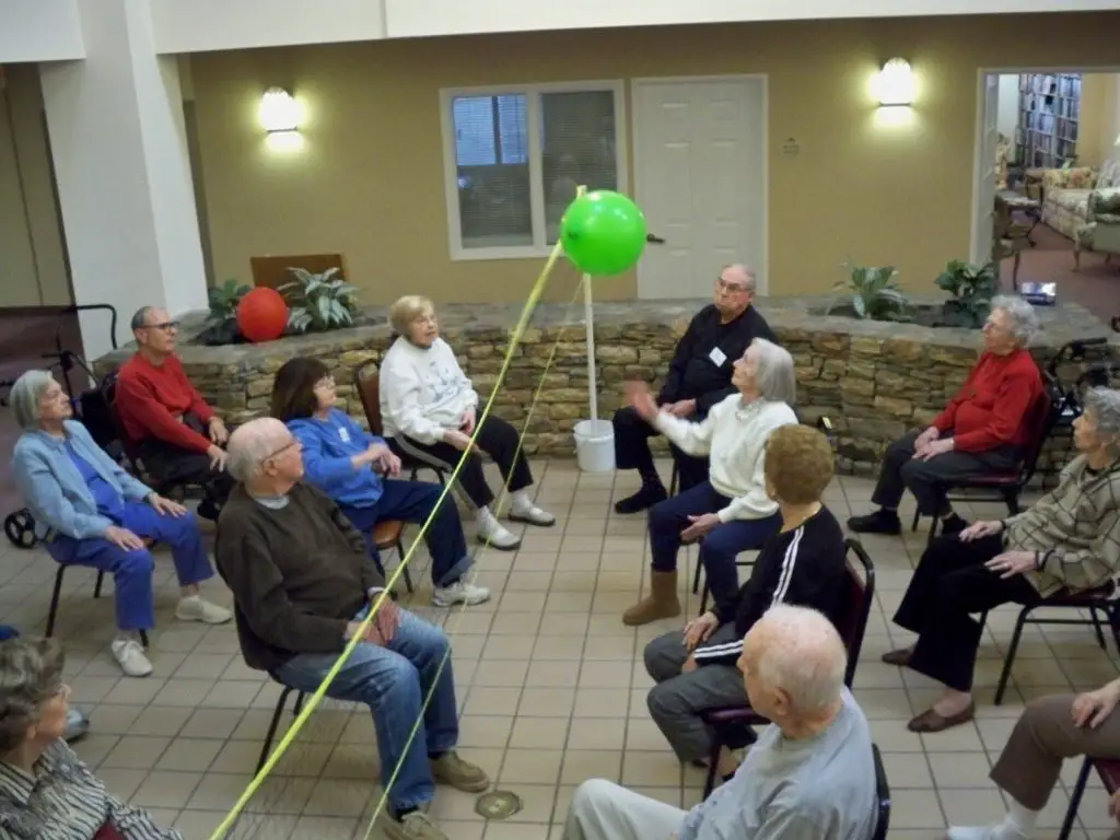 seniors enjoying a seated balloon volleyball in an aged care center
