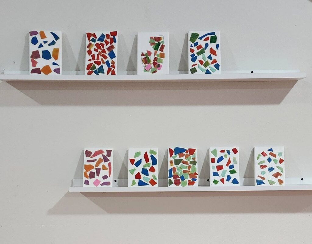Finished mosaic canvases made from painted lasagne pieces displayed on white picture-ledge shelves like a gallery wall
