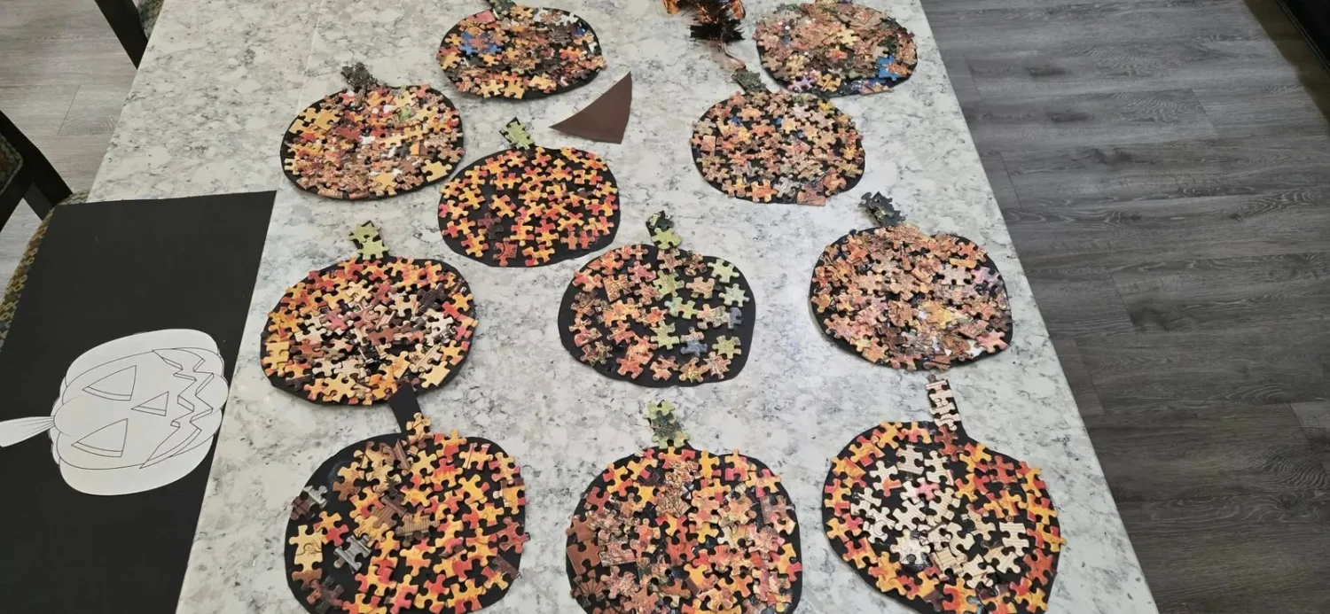 A table of finished puzzle piece pumpkins for Halloween made by residents in memory care, with autumn-coloured jigsaw pieces glued onto black card