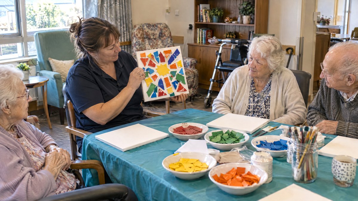 Activity coordinator showing residents a finished lasagne mosaic canvas before they start