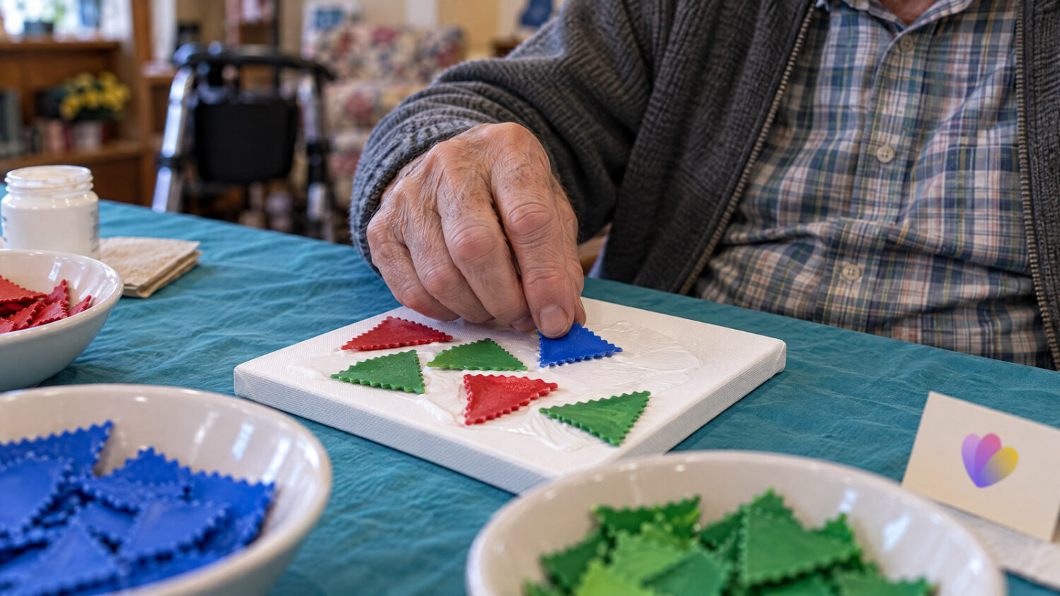 Aged care resident pressing coloured lasagne pieces onto a glued canvas