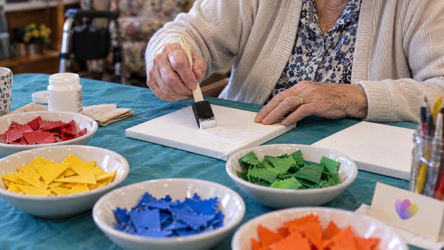 Aged care resident brushing glue onto a canvas for a lasagne mosaic craft